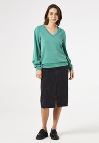 Pull en v teal à manches longues associé à une jupe midi en denim noir avec une fente à l'avant. Des chaussures à plateforme noires complètent le look.
