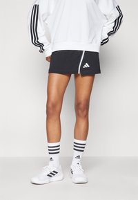 Svart träningskjol med vita detaljer, parat med en vit sweatshirt med svarta ränder på ärmarna. Vita sneakers och randiga strumpor.