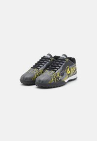 Zapatos deportivos en negro y gris con un empeine texturizado, que presentan un patrón abstracto amarillo, detalles en blanco y una suela de tracción de goma.