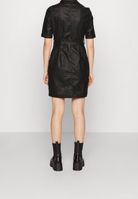 Czarna sukienka z krótkim rękawem, dopasowana w talii, o długości do kolan, gładkiej fakturze i akcentem w postaci paska. Noszona z masywnymi czarnymi botkami za kostkę.