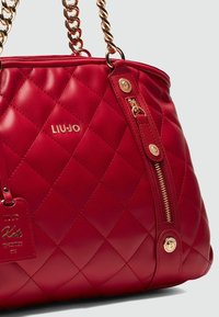 Rote gesteppte Lederhandtasche mit Kettenriemen, goldfarbenen Hardware und einer seitlichen Reißverschlusstasche. Mit einem Markenlogo und einem dekorativen Anhänger.