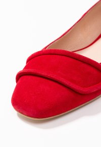 Rode suède instappers met een ronde neus, voorzien van een gestikte overlay-accent over de voorkant en een gladde binnenvoering.