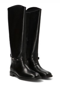 Botas altas de cuero negro con un acabado suave, que presentan un detalle de correa y mínimo metalizado. Suela plana, punta redonda, diseño estructurado.