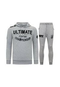 Grijze hoodie en bijpassende trainingsbroek met grote zwarte tekst en logo's. Zachte stof met een ontspannen pasvorm; de hoodie heeft een buidelzak.