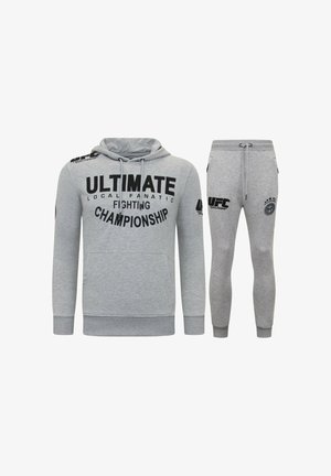 Grijze hoodie en bijpassende trainingsbroek met grote zwarte tekst en logo's. Zachte stof met een ontspannen pasvorm; de hoodie heeft een buidelzak.