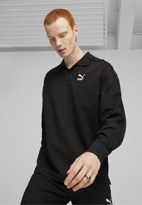 Must mustaga polo särk, millel on pikad varrukad ja tekstureeritud kangas, nööbiga krae ning vasakul rinnal valge Puma logo.