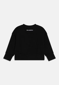 Melnā apgriezta sporta krekla jaka, kas izgatavota no mīksta auduma, ar apaļu kaklu un garām piedurknēm. Uz aizmugurējās kakla daļas ir drukāts "Karl Lagerfeld" logotips.