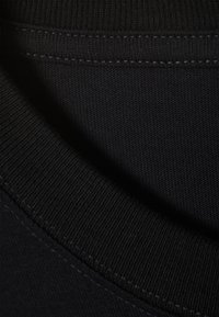 Teren de bumbac negru cu o textură netedă, cu guler rotund și margine ribbată. Accentuat de detalii de cusătură îngrijite.