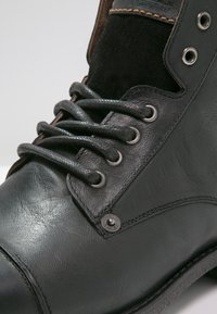 Stivaletto in pelle nera con accenti in suede, punta tonda, occhielli metallici e lacci piatti, caratterizzato da dettagli di cucitura a contrasto.