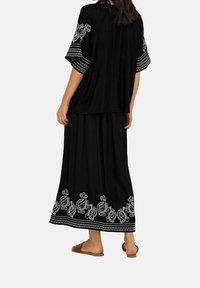 Conjunto negro de dos piezas que incluye una blusa de corte holgado con mangas bordadas y una falda larga adornada con patrones de paisley blancos.