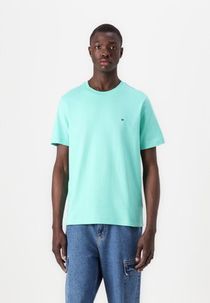 T-shirt vert menthe clair, en coton, col rond, manches courtes, avec un petit logo sur la poitrine, associé à un jean en denim bleu.