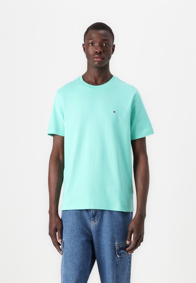 Lyse mintgrønn t-skjorte i bomullsmateriale, med rund hals og korte ermer, prydet med en liten logo på brystet, sammen med blå denimjeans.