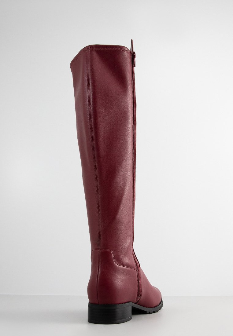 Stivale in pelle bordeaux alto con tacco nero basso, cerniera laterale e finitura liscia, fotografato su uno sfondo chiaro uniforme.