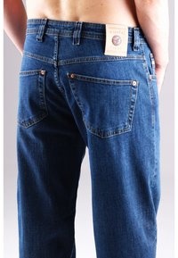 Dunkelblaue Denim-Jeans mit kupferfarbenen Nieten, einem Leder-Brandlabel und schrägen Gesäßtaschen. Die Jeans haben ein klassisches Design mit geradem Bein.