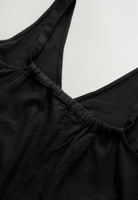 Débardeur noir avec des bretelles larges, une taille élastique froncée et un tissu doux et texturé. Design minimaliste avec une forme en V.