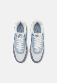 Nike Air Max tenisice s gornjim dijelom od svijetloplave i bijele mrežice, vezicama i gumene potplate s ljubičastim naglascima. Klasičan stil dizajna.