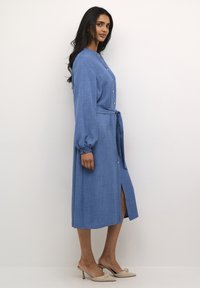 Blue, long-sleeve midi dress in lightweight fabric, featuring a buttoned front, tie belt at the waist, and a side slit.
