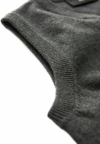 Grauer, gestrickter ärmelloser Oberteil mit glatter Textur, gerippten Kanten und einem runden Halsausschnitt. Enthält ein Etikett mit Markeninformationen.
