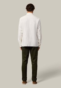 Camisa blanca de botones con mangas largas, hecha de un material suave, combinada con pantalones oscuros verdes. Textura suave, diseño de cuello simple.