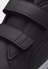 Μαύρο δερμάτινο αθλητικό παπούτσι με δύο φαρδιές, ραμμένες λουράκια με κλείσιμο τύπου χούκ και βρόχος και υφή εμφανής στην στρογγυλεμένη περιοχή της μύτης.