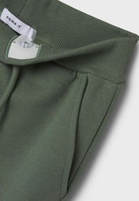 Grüne Baumwollmischung-Sweatpants mit geripptem Bund, Knopfverschluss und Seitentaschen, geprägt von einer glatten Textur und lässigem Design.