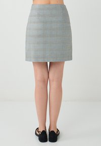 Jupe à carreaux gris et bleu, design ajusté, longueur au-dessus du genou, avec une texture lisse et des détails de couture subtils. Des chaussures noires complètent la tenue.