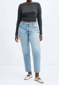 Vaaleanpesun denim-farkut suoran leikauksen kanssa, yhdistettynä istuvaan harmaaseen pitkähihanteiseen paitaan. Kengät ovat beigellä värillä varustetut kengät, joissa on remmi jalan yli.