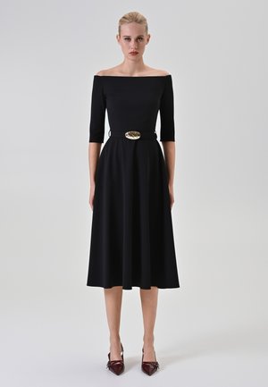 Black off-the-shoulder dress with three-quarter sleeves, fitted bodice, flowing skirt, and a gold belt buckle. Features a smooth texture.