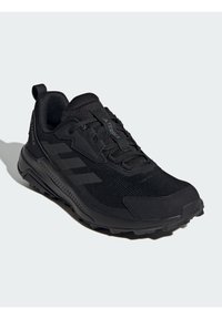 Chaussure de sport noire avec une tige en maille texturée, un bout renforcé, une semelle en caoutchouc et un design à trois bandes emblématique sur le côté.
