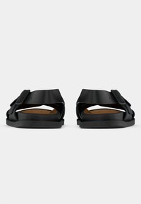 Μαύρα σανδάλια με φαρδιά λουρί και ρυθμιζόμενο αγκράφα, με μαλακό πάτο και επίπεδη λαστιχένια σόλα. Μινιμαλιστικός σχεδιασμός, χωρίς σχέδια.