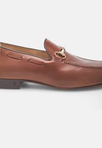 Mocassins en cuir brun avec un bout arrondi, des coutures décoratives et des accents en métal doré à l'avant ; petit talon en bois.