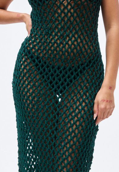 Πράσινο πλεκτό φόρεμα με σχεδιασμό δίχτυ, που παρουσιάζει ανοιχτό πλέξιμο, εφαρμοστή σιλουέτα και απαλό υφή. Διαθέτει σκίσιμο μέχρι το μπούτι.