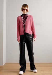 Rožinis megztinis suknelė virš juodos ir baltos raštuotos bluzės, derinama su juodais odiniais kelnėmis ir baltais sportbačiais. Modelis dėvi rožinius akinius nuo saulės.