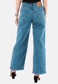 Jeans a gamba larga di colore blu chiaro in denim con vita alta, caratterizzati da tasche posteriori con cuciture distintive e una patch in pelle con il logo del marchio.