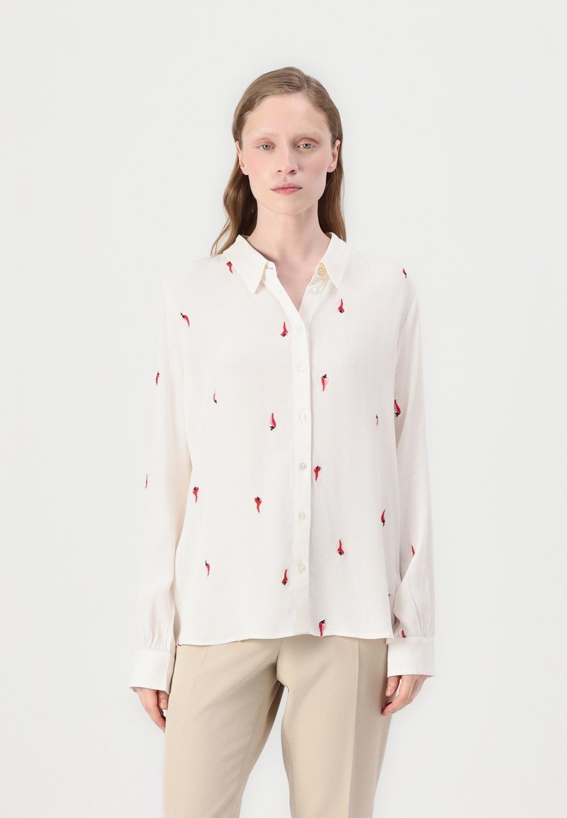 White long-sleeve shirt with red and black embroidered patterns, button-up front, and a classic collar. Smooth fabric with relaxed fit.