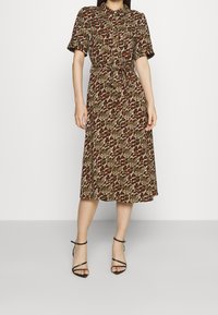 Abito camicia con stampa animalier marrone, crema e rossa. Caratterizzato da maniche corte, cintura in vita e lunghezza a metà polpaccio. Tacchi neri con cinturini.