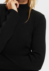 Schwarzer gerippter Rollkragenpullover mit langen Ärmeln, ausgestattet mit einem figurbetonten Design und weichem Material. Nahaufnahme des Kragens und des Ärmels.