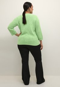 Maglione lavorato a maglia verde chiaro con motivo a diamante testurizzato e maniche tre quarti, abbinato a pantaloni neri a campana.