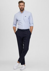 Lichtblauw en wit gestreept overhemd met knopen, gecombineerd met donkere marineblauwe broek en witte sneakers, met een borstzak en opgerolde mouwen.