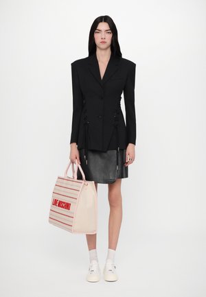 Zwarte gestructureerde blazer met zijkoorden, gecombineerd met een zwarte leren rok. Draagt een beige tas met roze accenten en een rood logo. Witte sneakers.