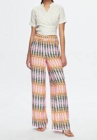 Haut blanc croisé à manches courtes associé à un pantalon rose ample avec des motifs de pois verts et oranges. Texture lisse, coupe décontractée.