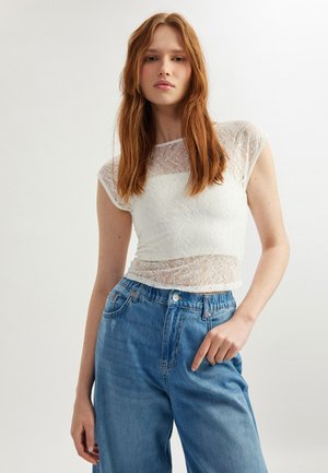 Witte kanten top met korte mouwen, met een doorschijnende overlay en een aansluitend ontwerp, gecombineerd met losse blauwe denim jeans.