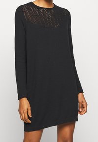 Robe noire à manches longues avec un motif en maille texturée sur le haut, un col rond et un ourlet côtelé. Confectionnée dans un matériau doux et léger.