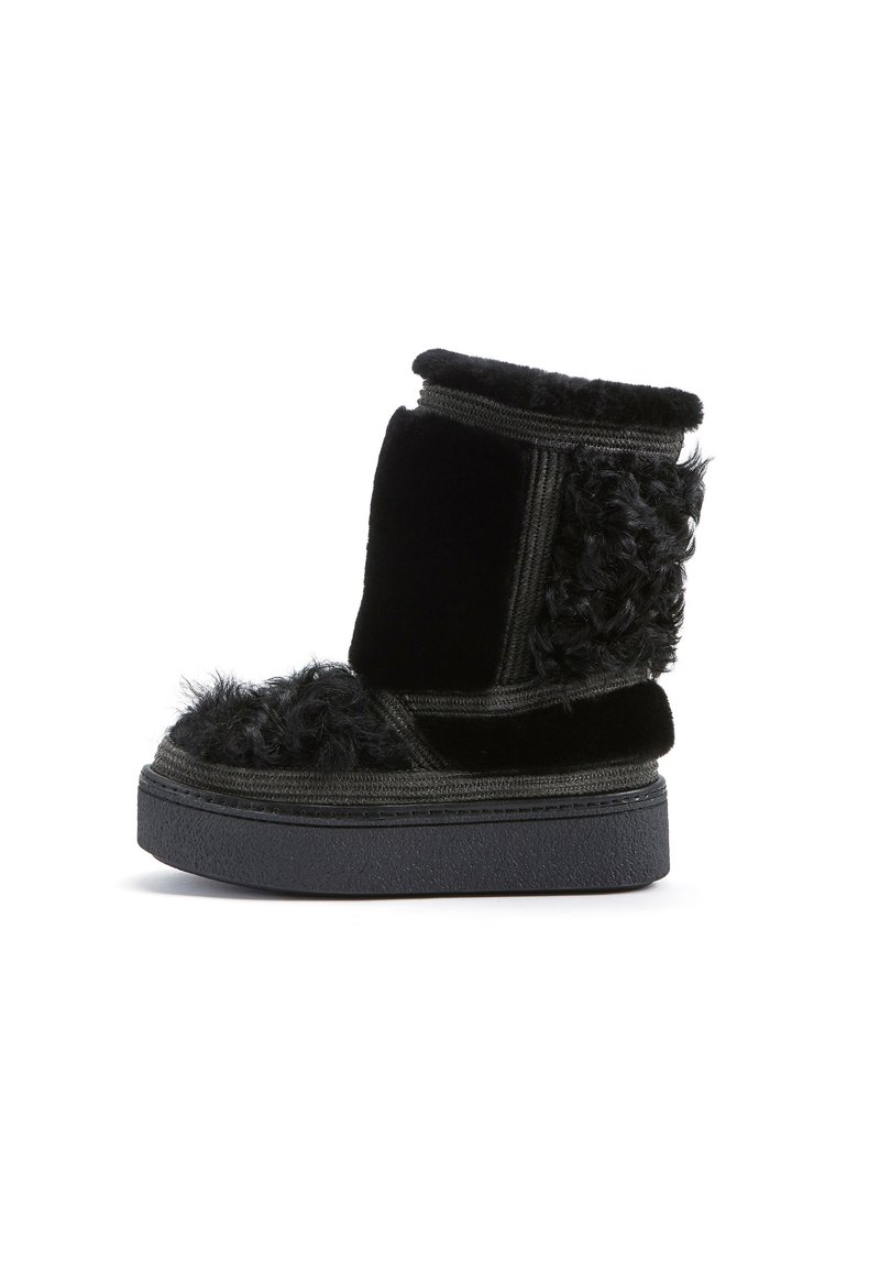 Stivaletto alla caviglia foderato in pelliccia nera con una parte superiore testurizzata, dotato di una suola nera spessa e dettagli in tessuto a contrasto, inclusi texture lisce e soffici.