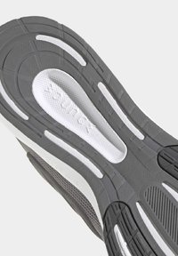 Suola di sneaker grigia con motivi testurizzati, accenti bianchi e caratteristiche di ammortizzazione. Scanalature circolari e striature per la trazione.