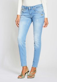 Jeans ajustados de denim en azul claro, con ligero desgaste, ajuste de tiro medio, bolsillos frontales y un botón con marca.
