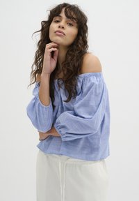 Blauw en wit gestreepte off-the-shoulder blouse met luchtige mouwen, gecombineerd met lichtgekleurde, loszittende broek. Eenvoudig ontwerp, lichtgewicht stof.