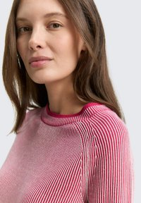 Sweter w paski w odcieniach różu i bieli, z okrągłym dekoltem i miękką teksturą, podkreślający dopasowany krój.