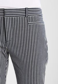 Pantaloni a righe blu navy e bianchi realizzati in tessuto testurizzato; presentano una vita con passante per cintura e una tasca posteriore.