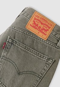 Πίσω τσέπη γκρι τζιν με κόκκινη ετικέτα Levi's και καφέ δερμάτινο πατς λογότυπο Levi Strauss & Co. που δείχνει δύο άλογα και κείμενο.